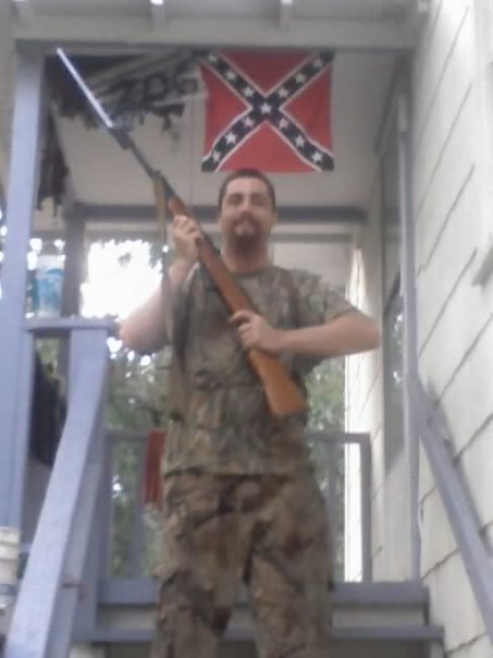 John Paul Cupp with SKS rifle in 2009 with confederate flag in the background. Photo taken in 2009 while he was advocating white supremacy and head of the official U.S. Songun Politics Study Group